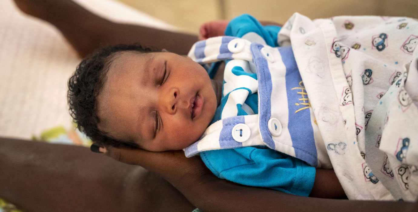 A baby sleeps peacefully in the arms of its caregiver.